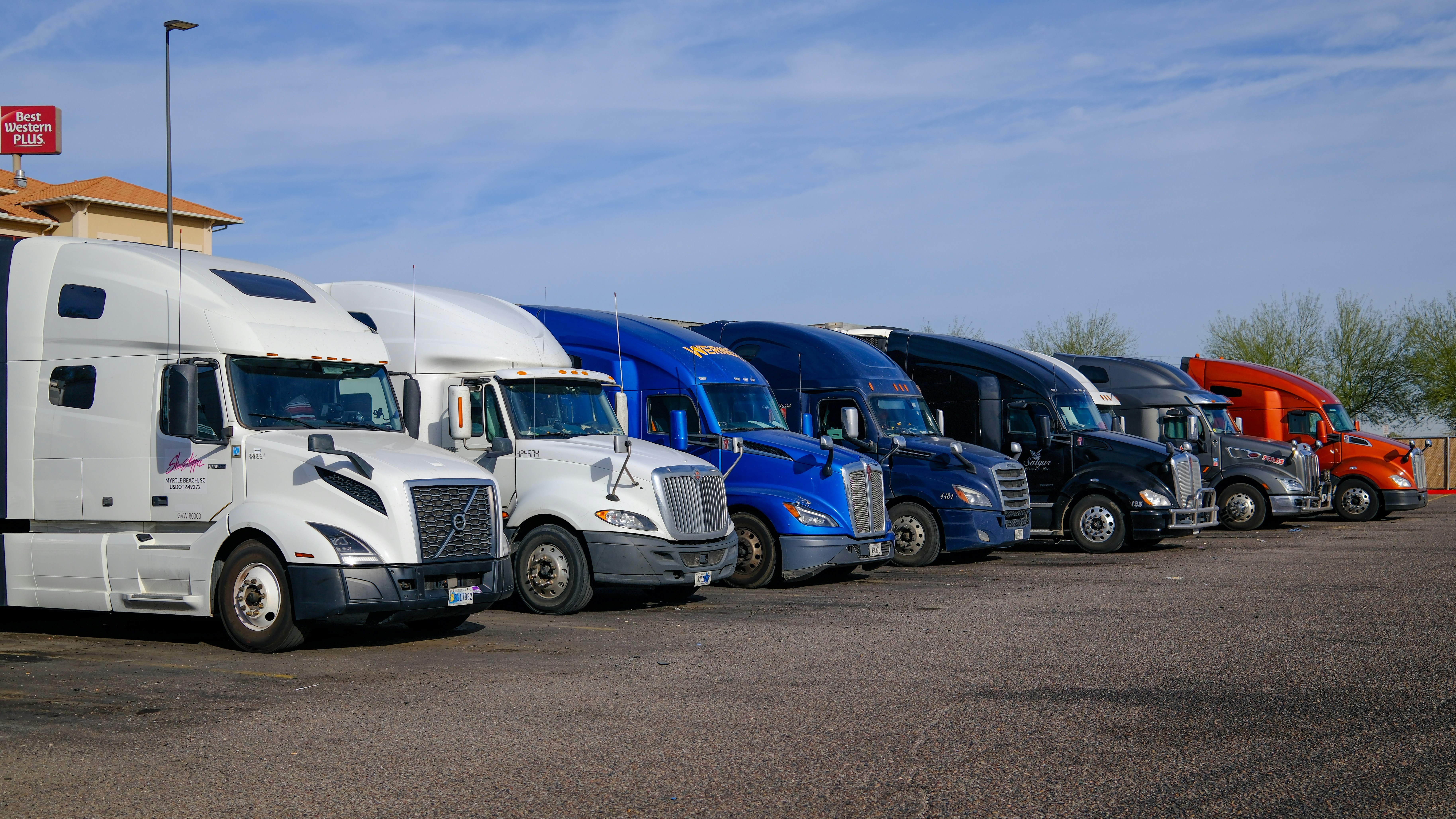 Row of American long-haul semi trucks parked at a logistics facility